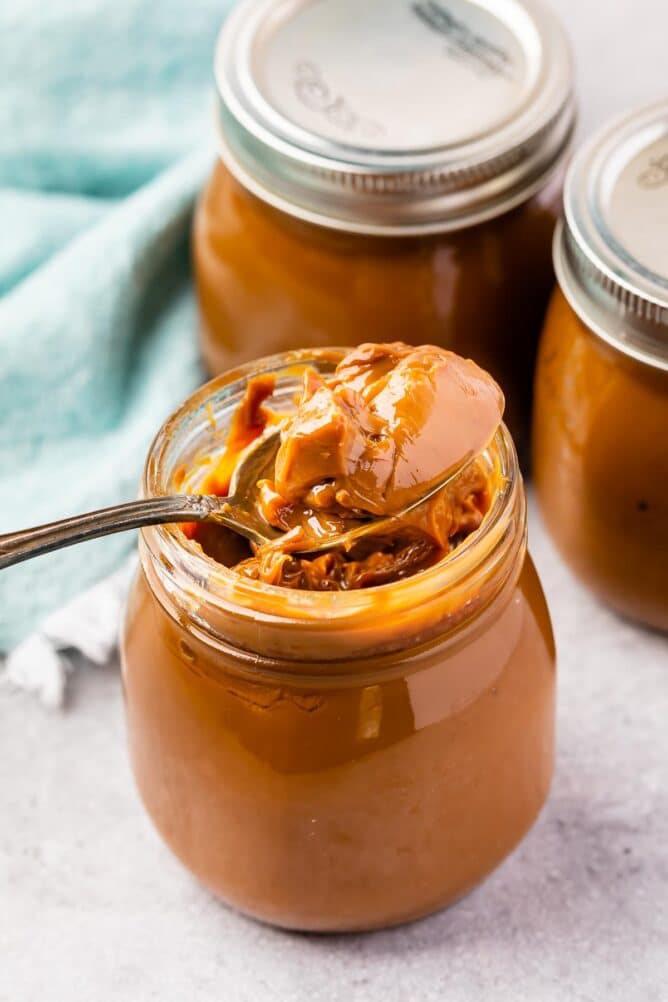 One spoon inside jar of dulce de leche with more jars in background