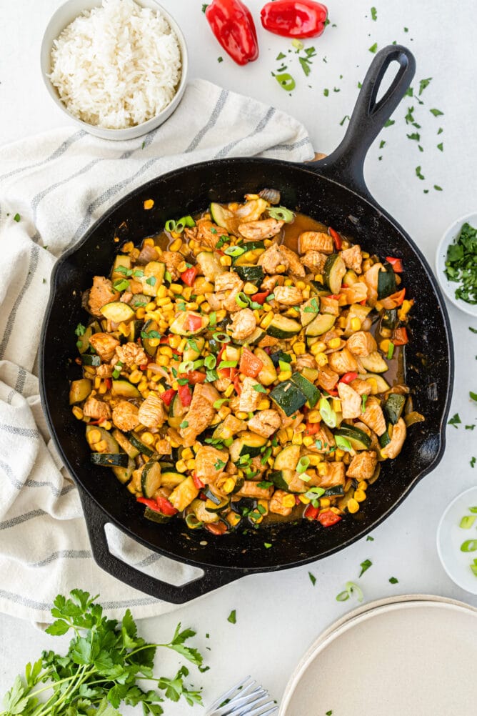 Overhead shot of bbq chicken skillet in cast iron skillet with more ingredients around it