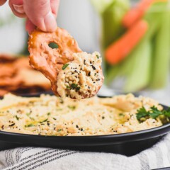 Pretzel chip being dipped into the everything hummus