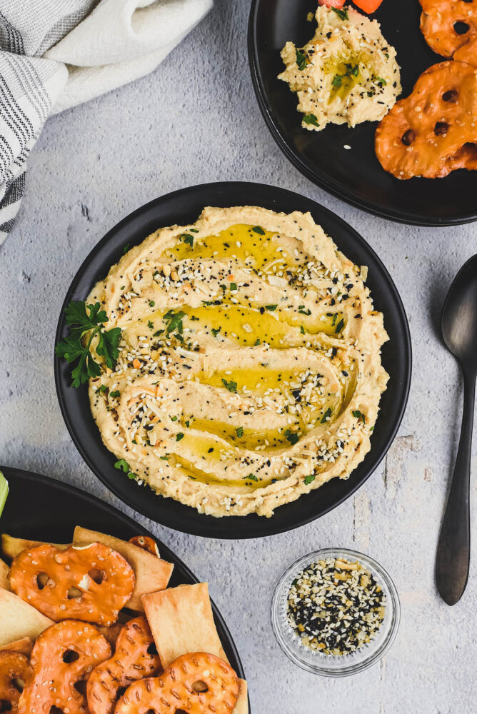 Overhead shot of everything hummus in a bowl next to bowls of pretzel chips