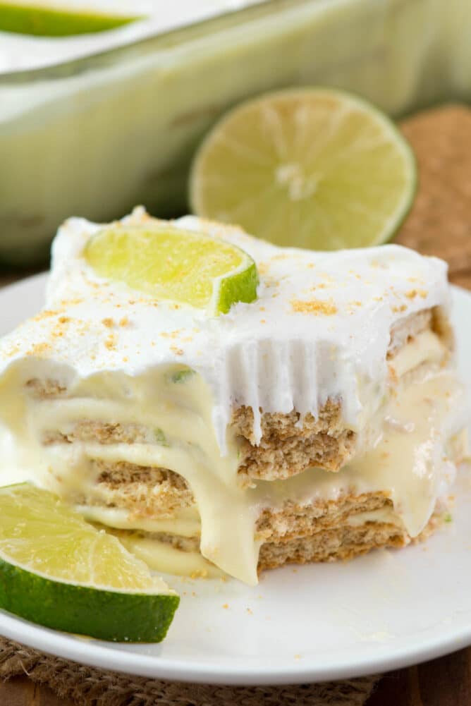 One slice of key lime eclair on a plate topped with lime wedges missing one corner bite