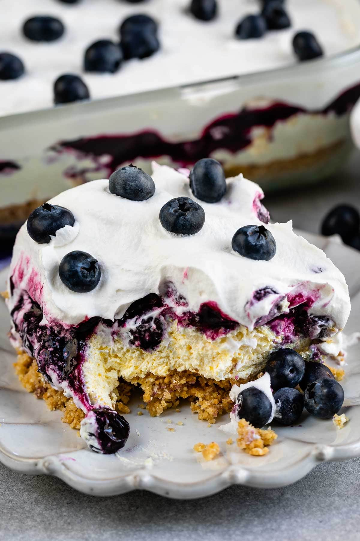 One large square slice of blueberry delight lush on a plate with one corner bite missing
