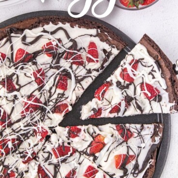 Overhead shot of brownie pizza with one slice being pulled away from the full pizza with recipe title on top of image