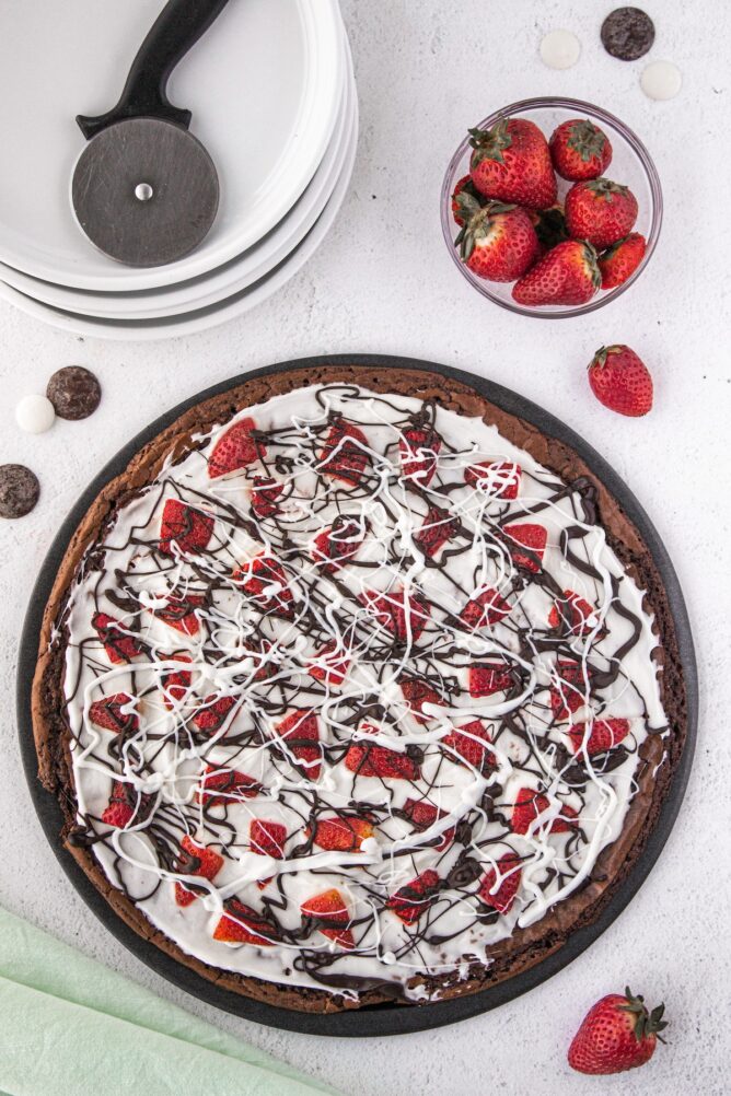 Overhead shot of brownie pizza next to a cup of strawberries