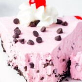 One large slice of cherry jello pie topped with chocolate chips, whipped cream and cherry with first bite missing and recipe title on top of image