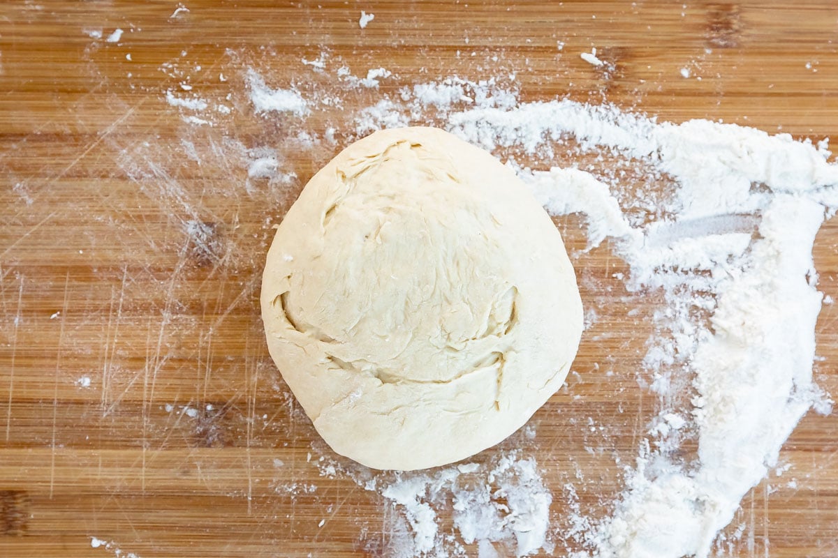 Pizza dough on a wooden cutting board with flour