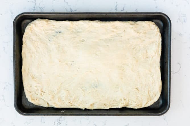 Pizza dough spread out on a sheet pan