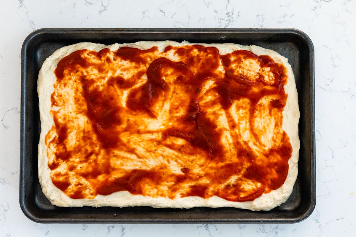 Pizza dough topped with sauce on a sheet pan