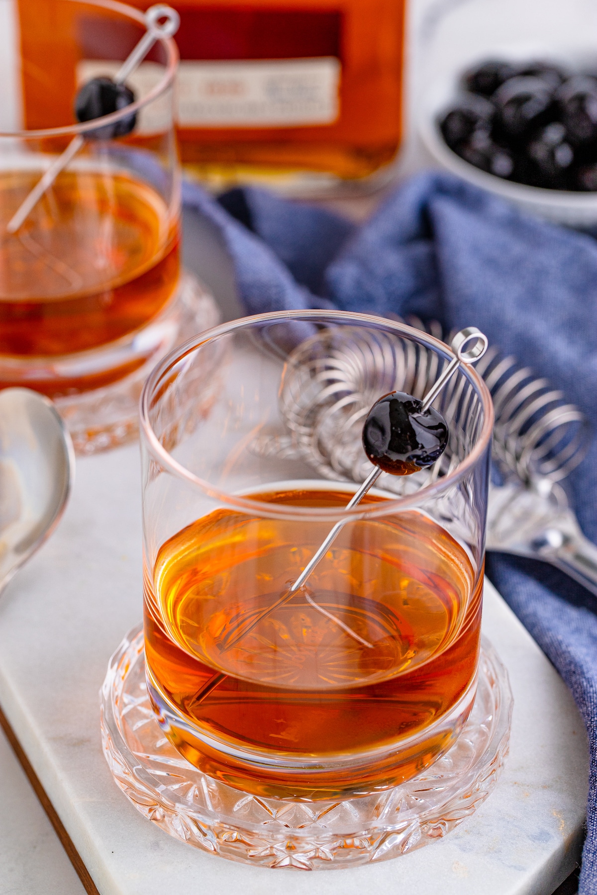 Two manhattan cocktails with mixing ingredients in background