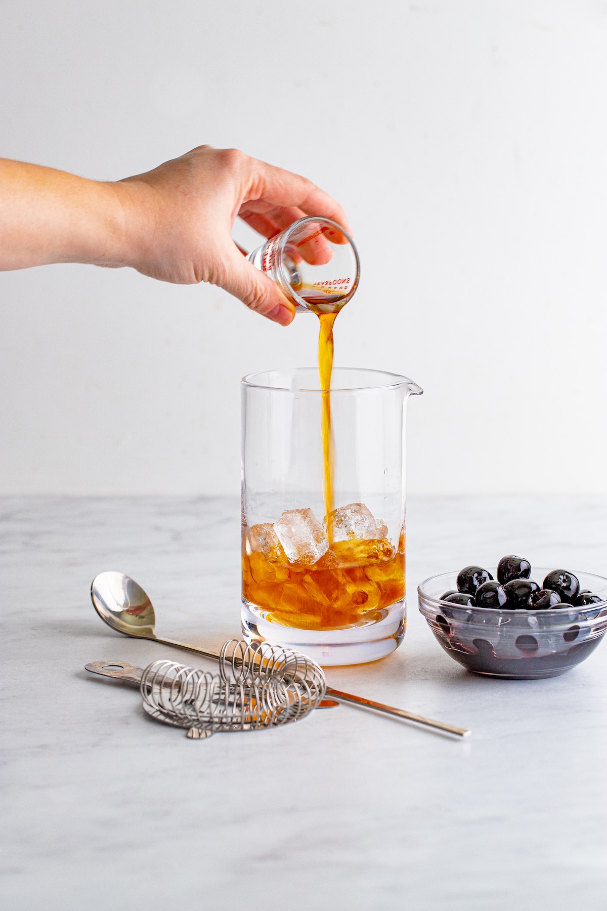 Shot being poured into pitcher while making manhattans