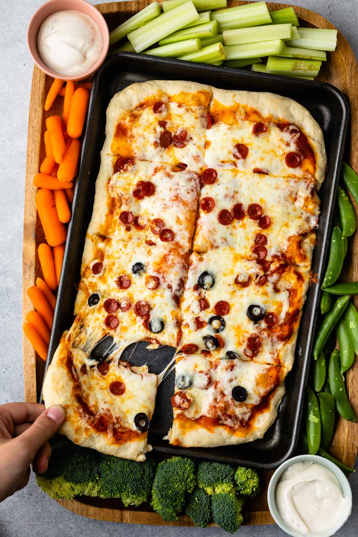 Overhead shot of sheet pan pizza on a wooden cutting board surrounded by veggies