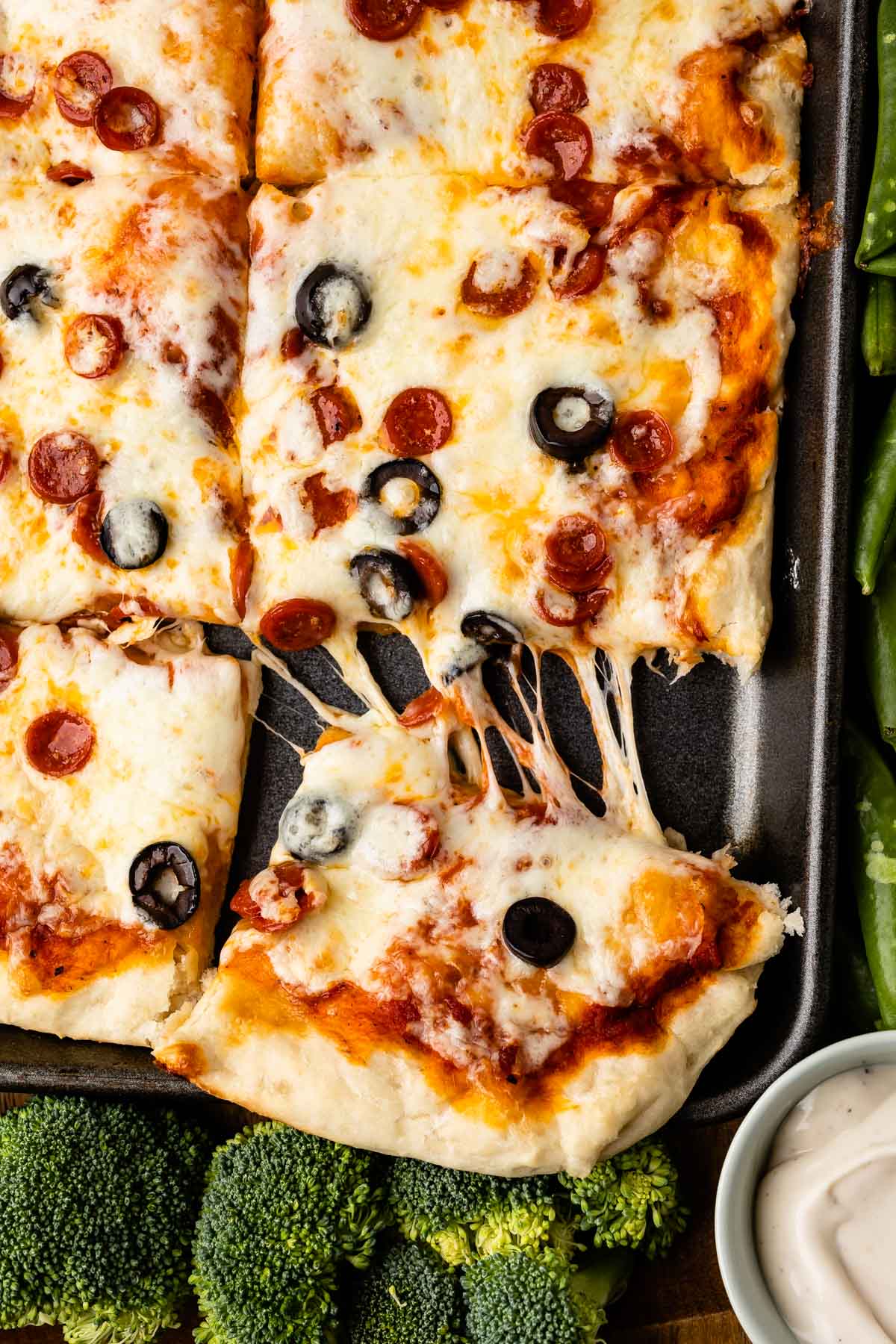 Close up shot of sheet pan pizza with corner piece pulled away from rest of pizza