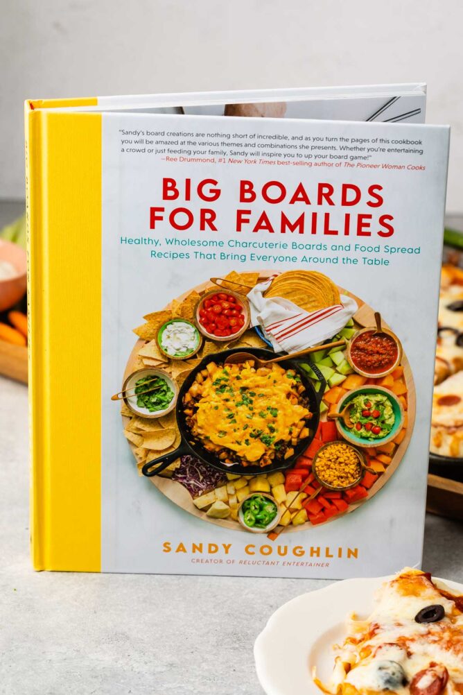 Big board for families book standing up on counter next to plate of pizza