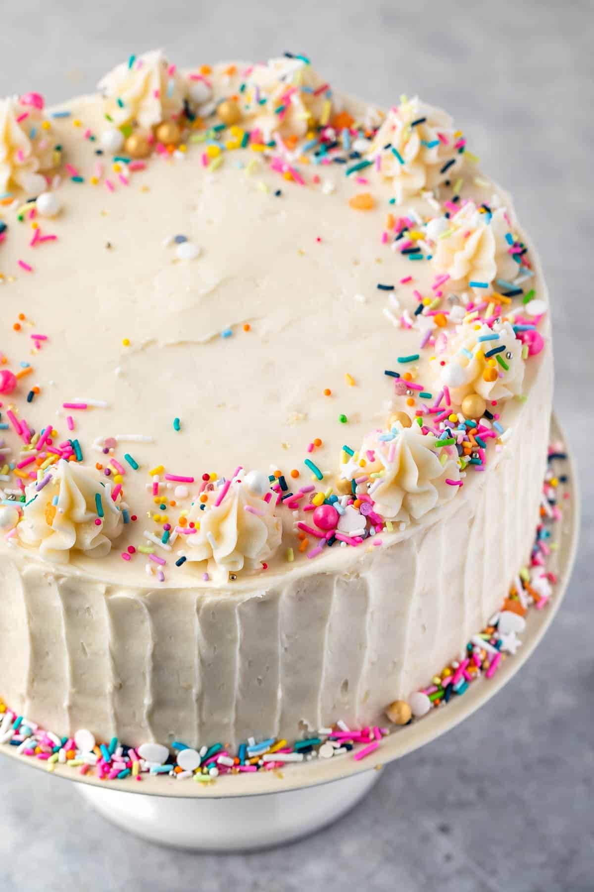 cake with vanilla frosting and sprinkles on white cake plate.