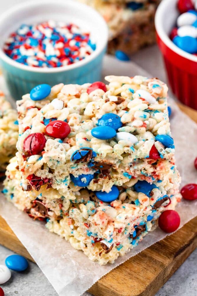 Two 4th of july rice krispie treats stacked on top of eachother with more sprinkles and M&Ms in background