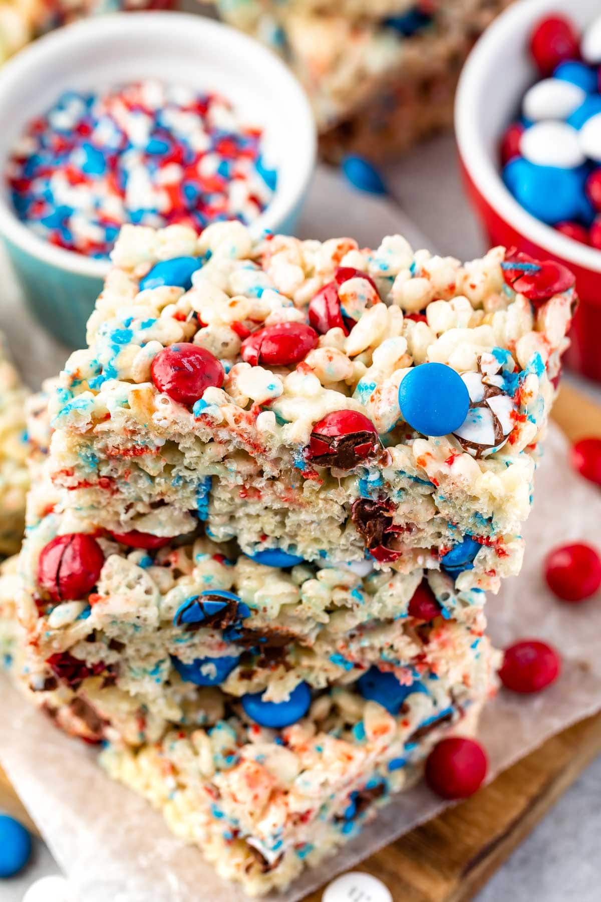 Two 4th of july rice krispie treats stacked on top of eachother with more sprinkles and M&Ms in background