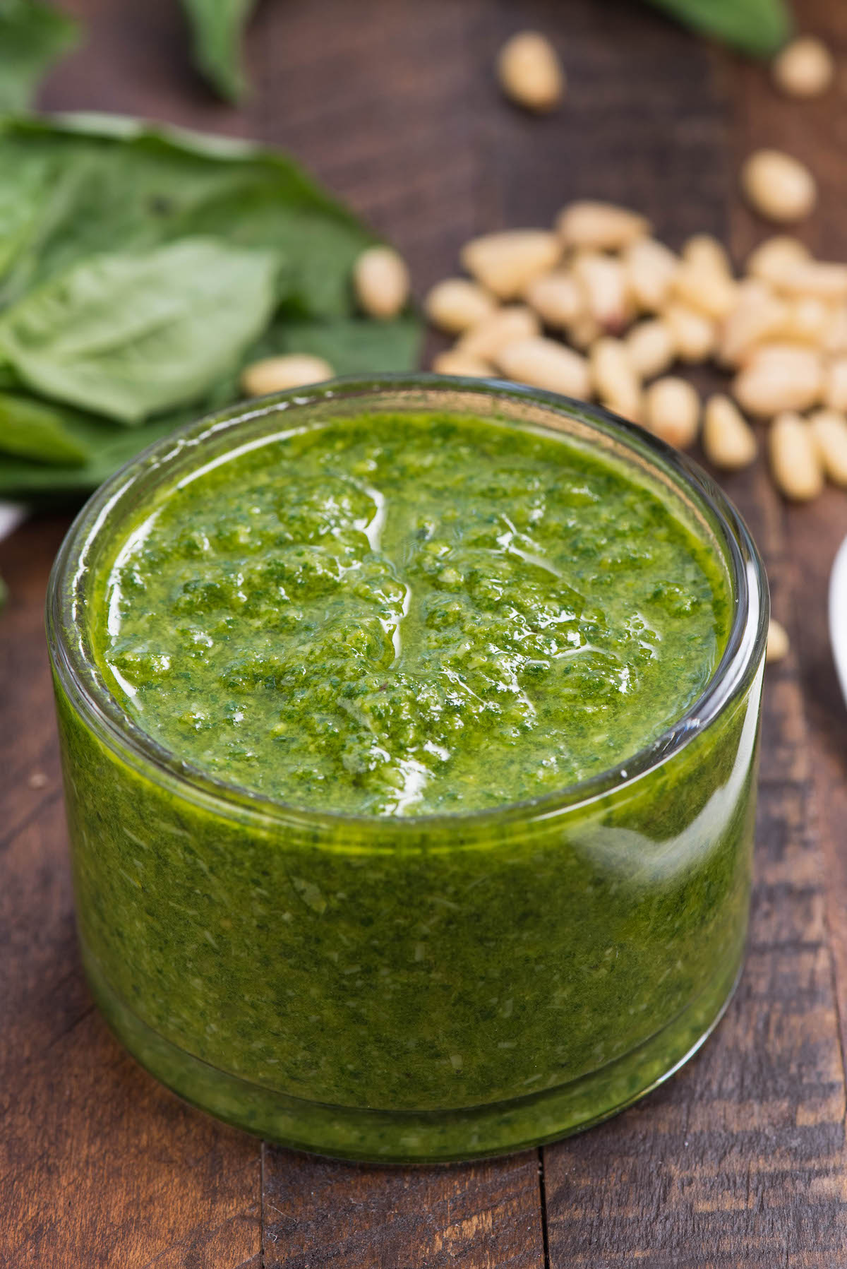 Small glass dish of easy basil pesto with pine nuts and basil leaves behind it