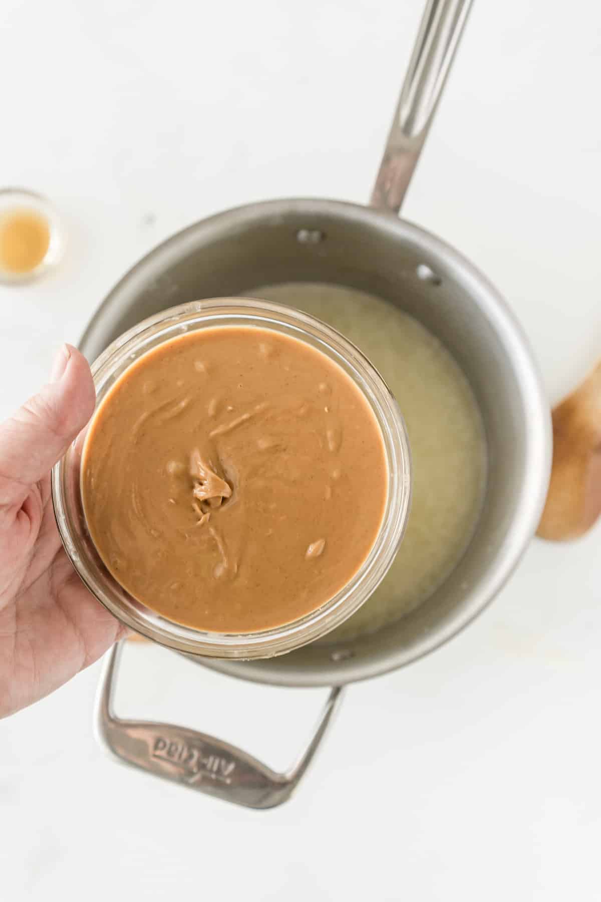 hand holding bowl of peanut butter over saucepan.