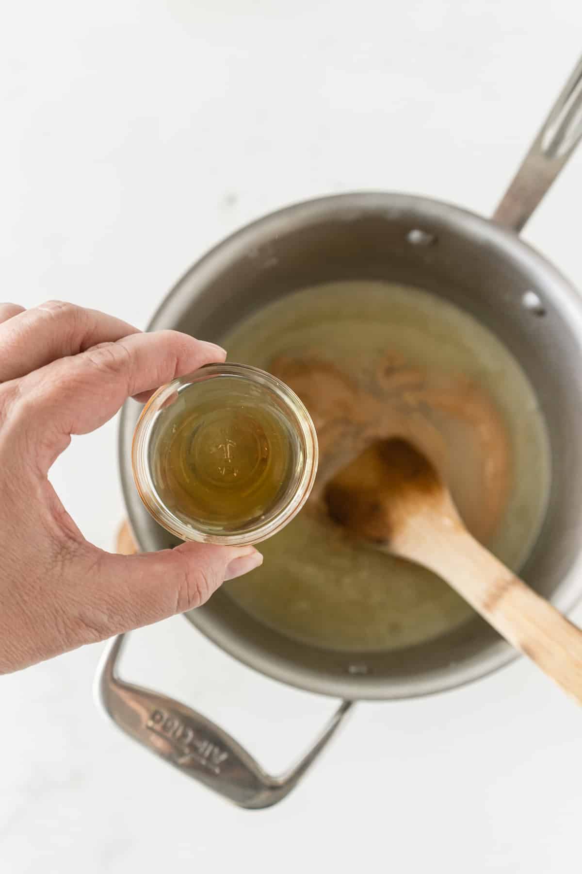 hand holding bowl of vanilla over saucepan.