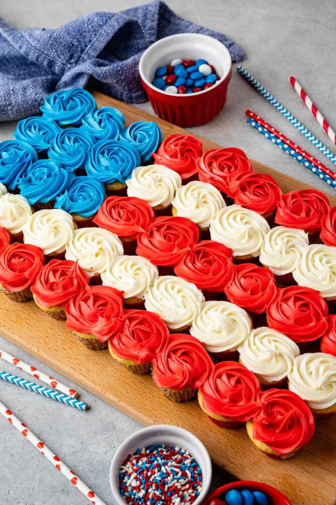 Overhead shot of american flag cupcake cake next to patriotic toppings and straws
