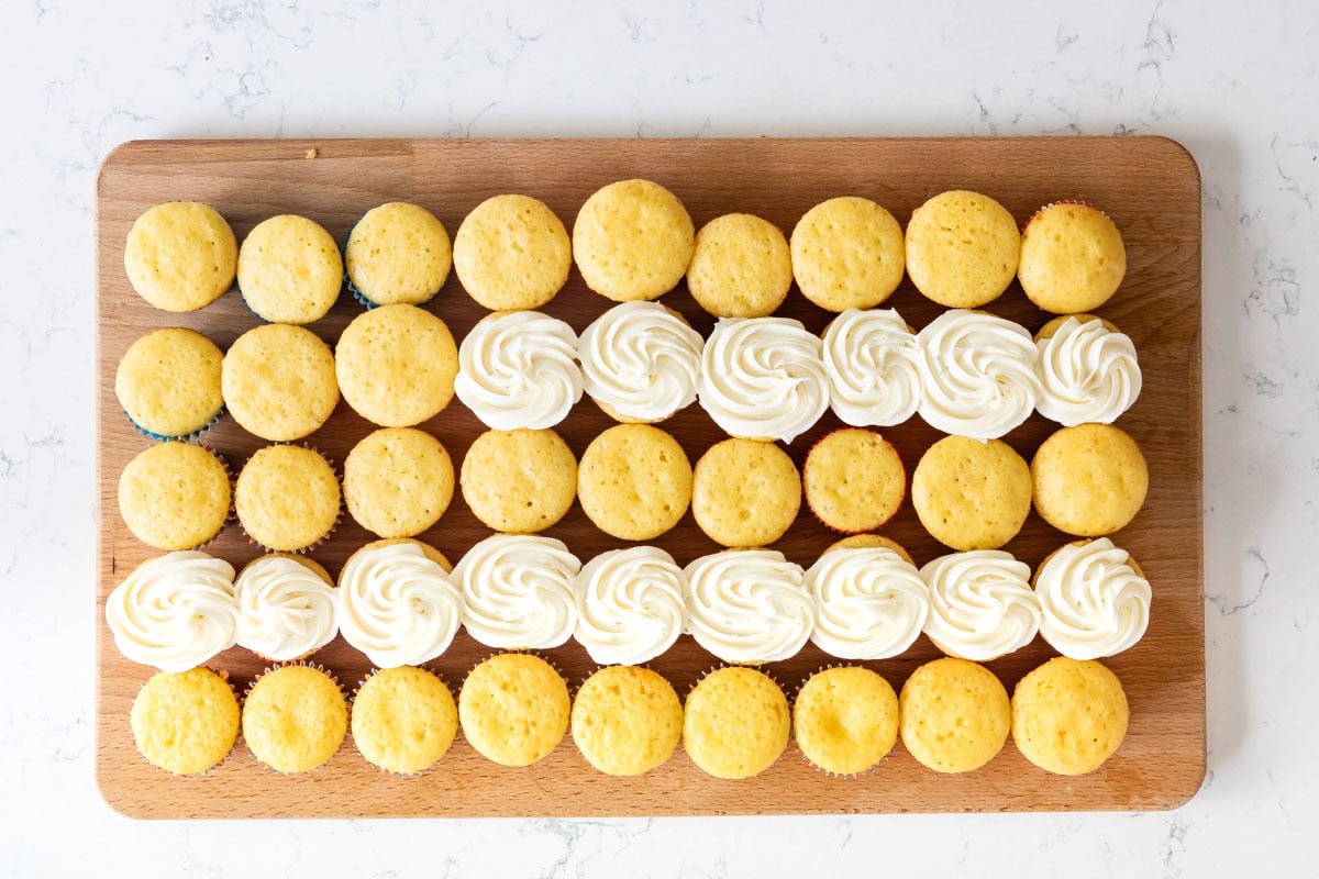 Overhead shot of vanilla cupcakes on cutting board with two rows decorated with white frosting