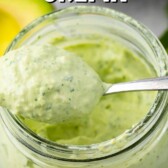 Overhead shot of avocado cilantro crema in a small mason jar with spoon coming out of jar with recipe title on top of image