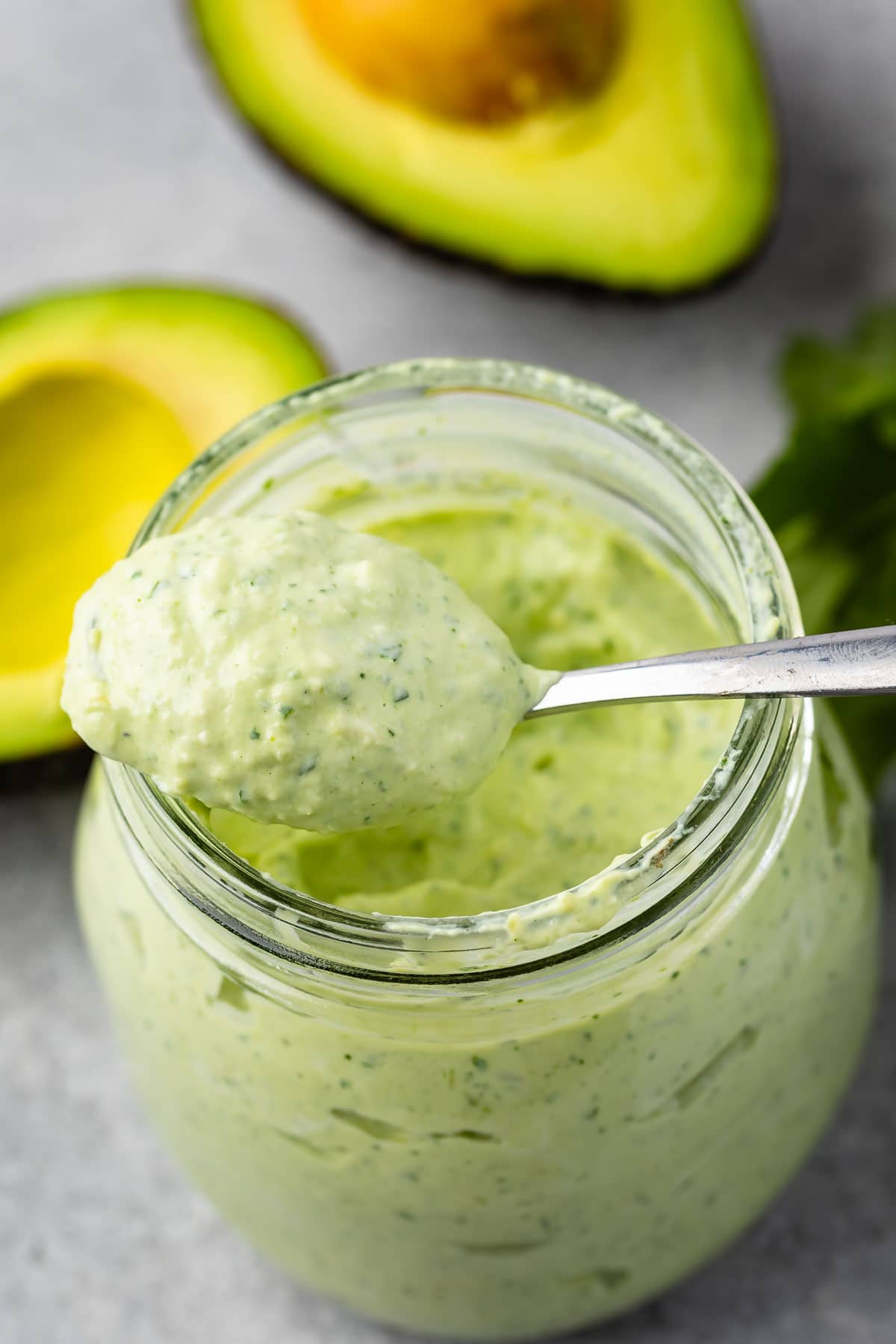 Overhead shot of avocado cilantro crema in a small mason jar with spoon coming out of jar