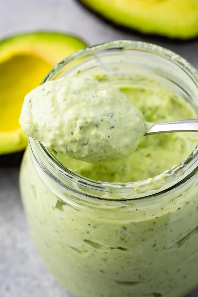 Overhead shot of avocado cilantro crema in a small mason jar with spoon coming out of jar