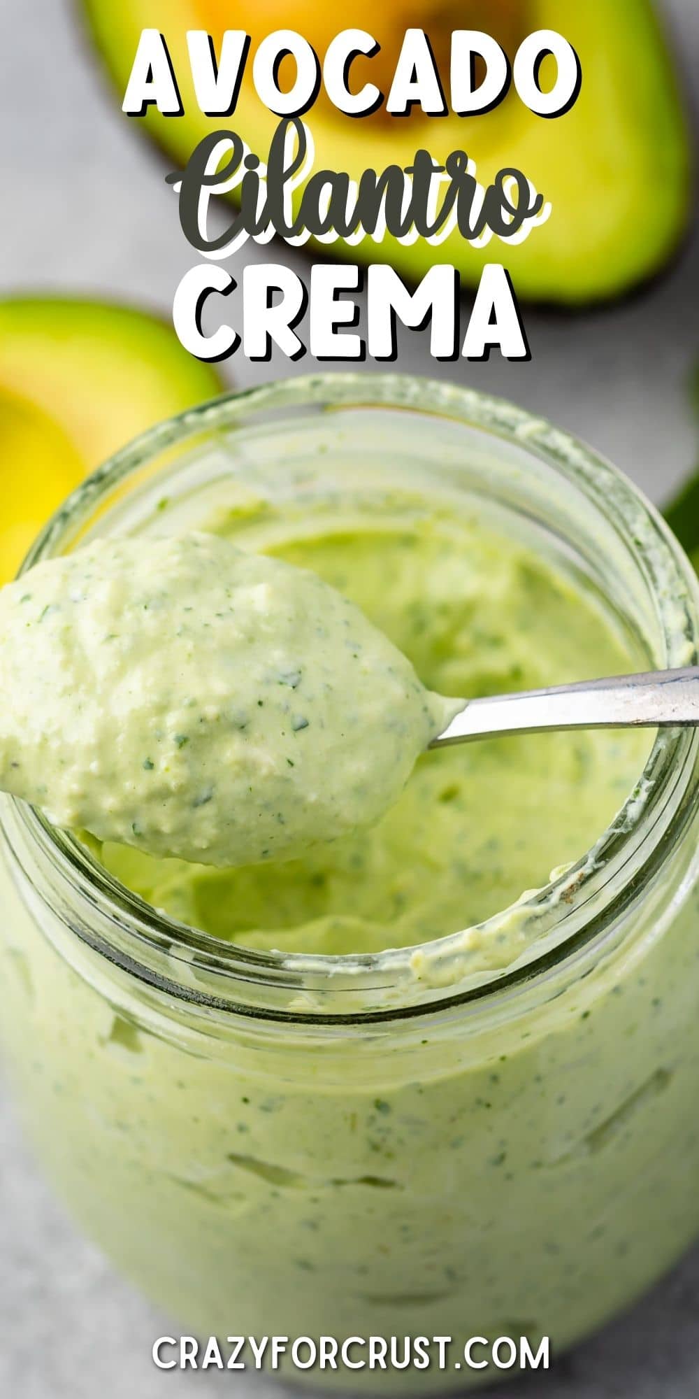 Overhead shot of avocado cilantro crema in a small mason jar with spoon coming out of jar with recipe title on top of image
