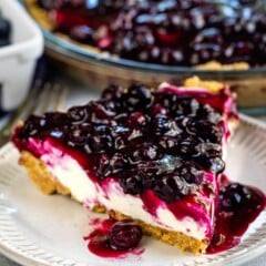 One slice of blueberry cream cheese pie on a plate with rest of pie behind it