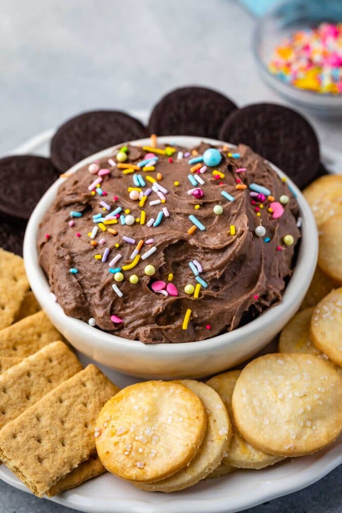 Cake batter dip in a bowl topped with sprinkles and surrounded by dippers