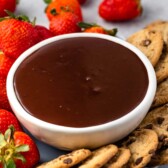 Chocolate dip in a bowl surrounded by chocolate chip cookies and strawberries
