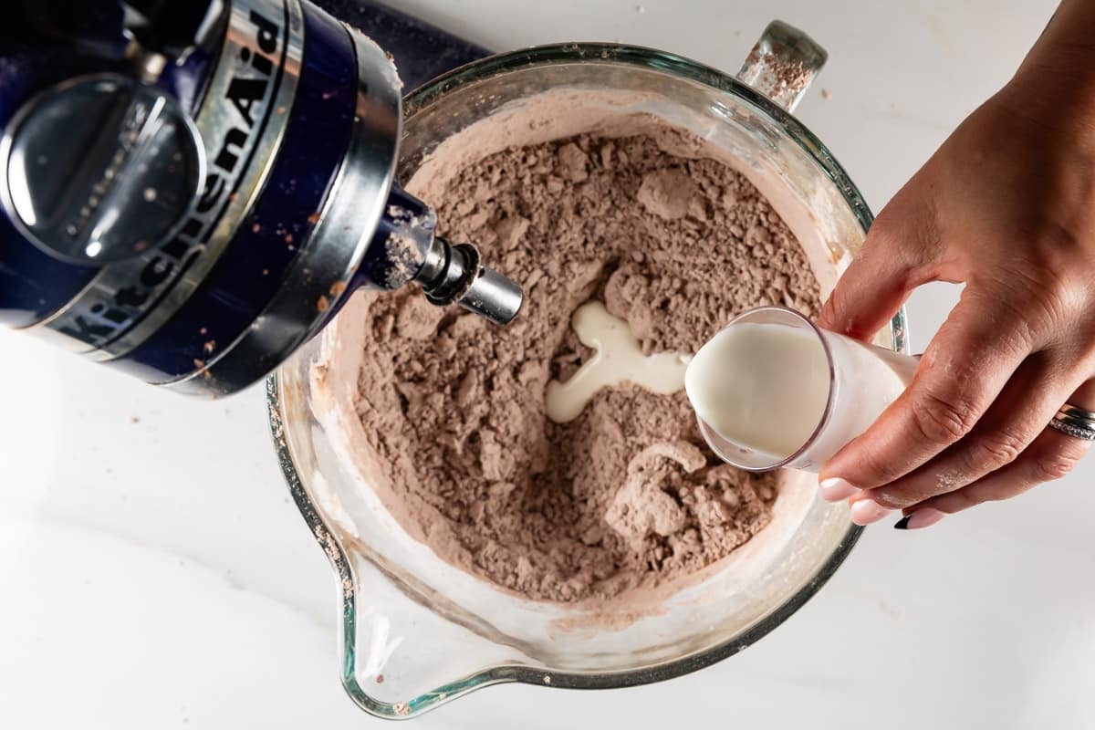 hand pouring milk into mixer with cocoa.