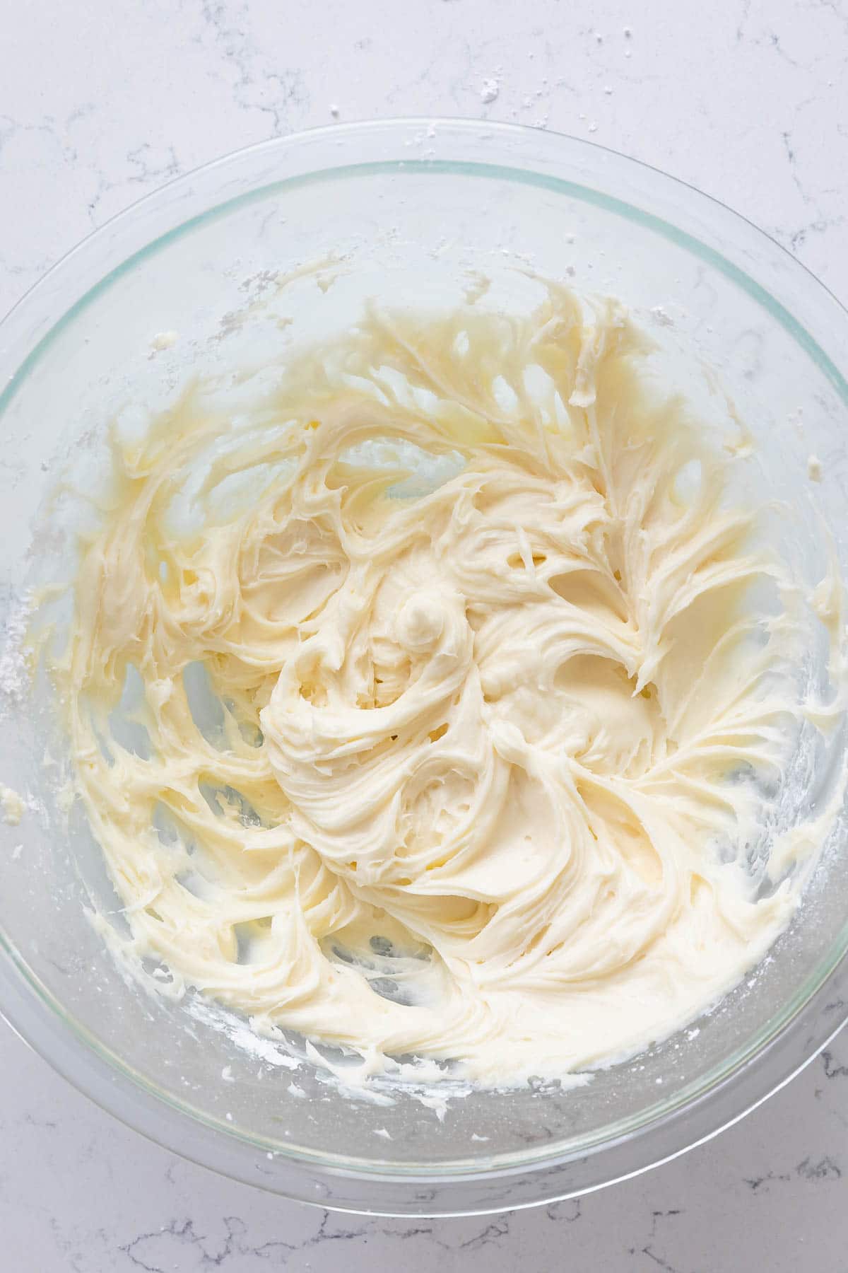Overhead shot of cream cheese frosting in glass mixing bowl