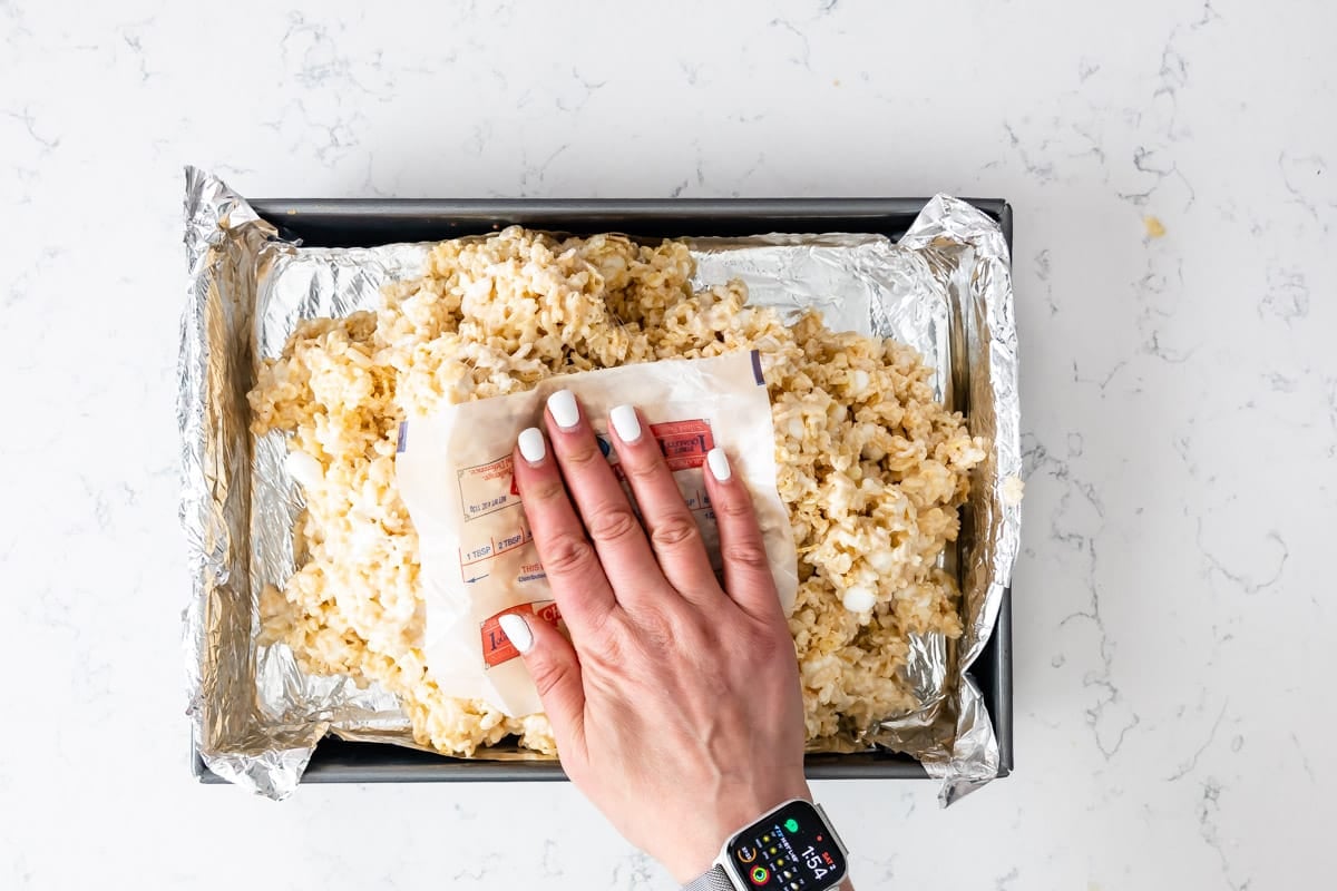 hand pressing krispie treats in 9x13 pan using butter liner.