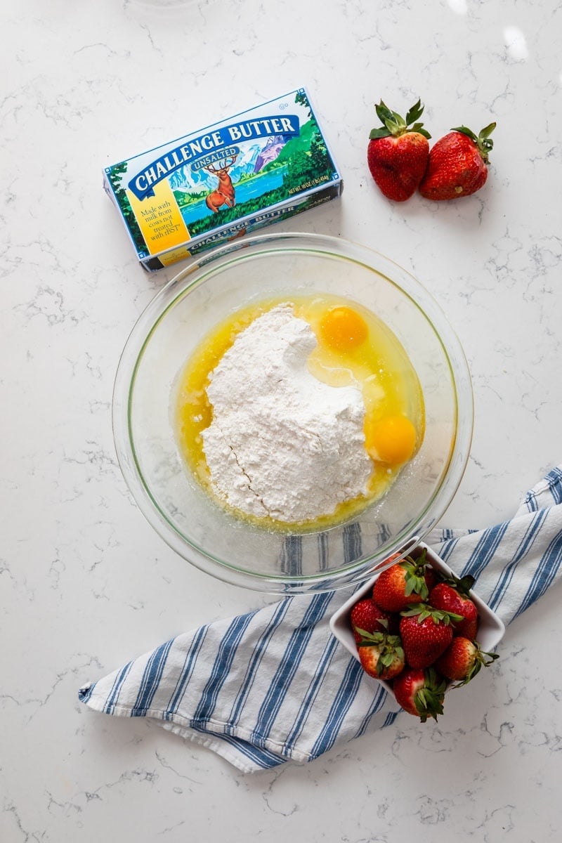 cake mix, eggs, and butter in large bowl with butter box and berries around.