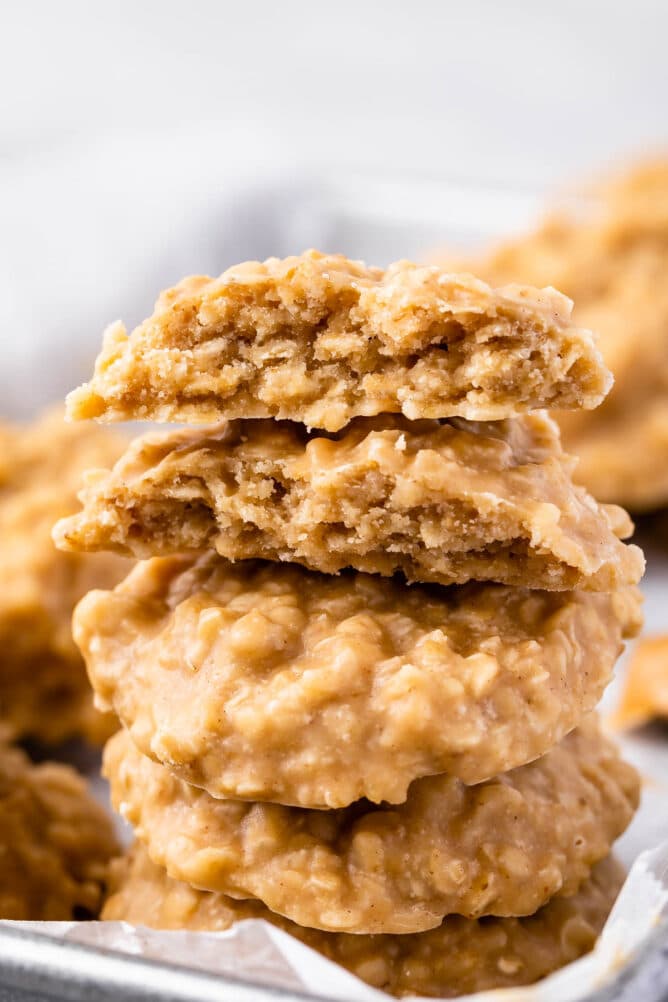 Four no bake peanut butter cookies stacked on top of eachother with top one split in half to show inside of cookie