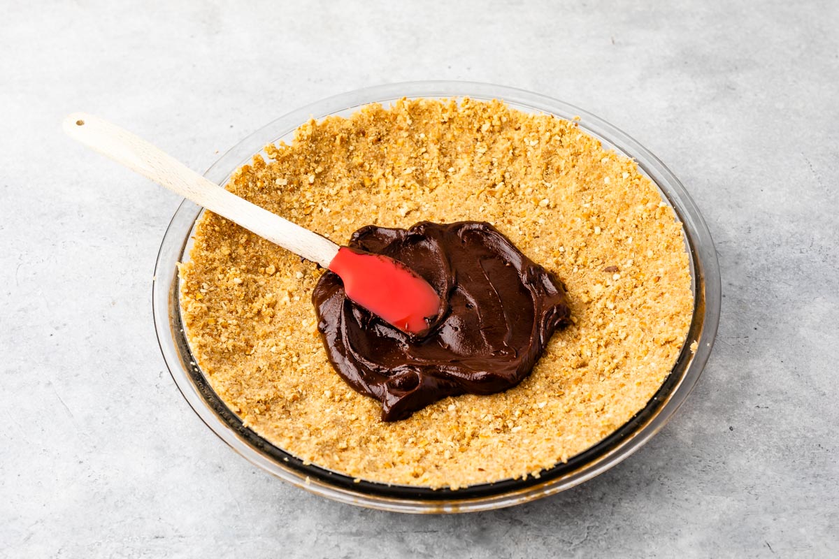 Chocolate ganache being spread onto pretzel crust