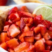 Bowl of strawberry salsa with a lime wedge surrounded by pie crust chips and recipe title on top of image
