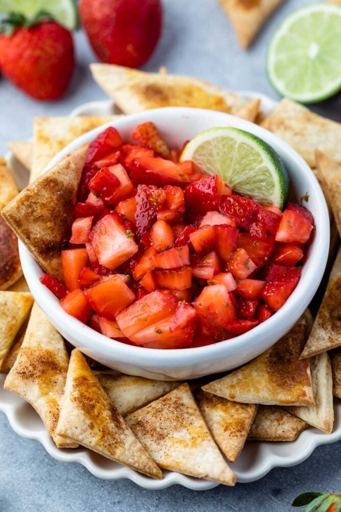 Bowl of strawberry salsa with a lime wedge surrounded by pie crust chips