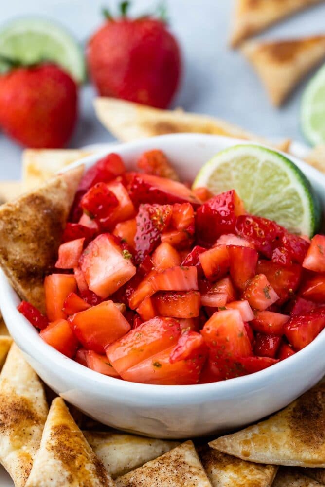 Bowl of strawberry salsa with a lime wedge surrounded by pie crust chips