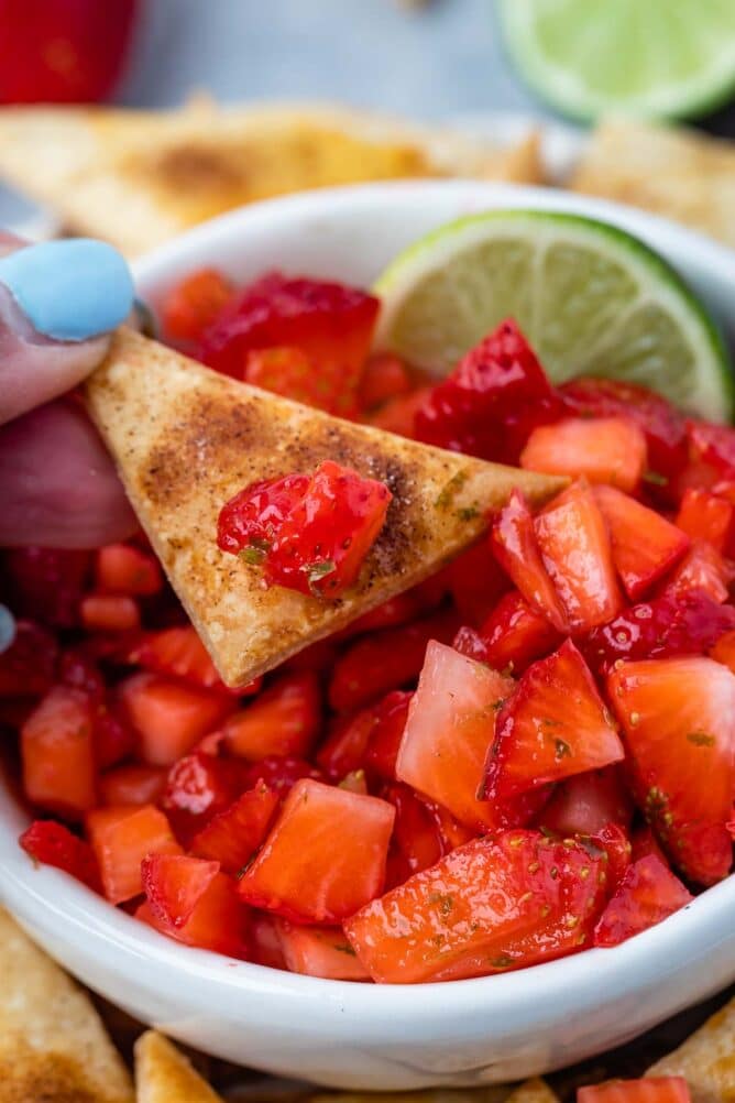 Pie crust chip scooping out strawberry salsa from a bowl