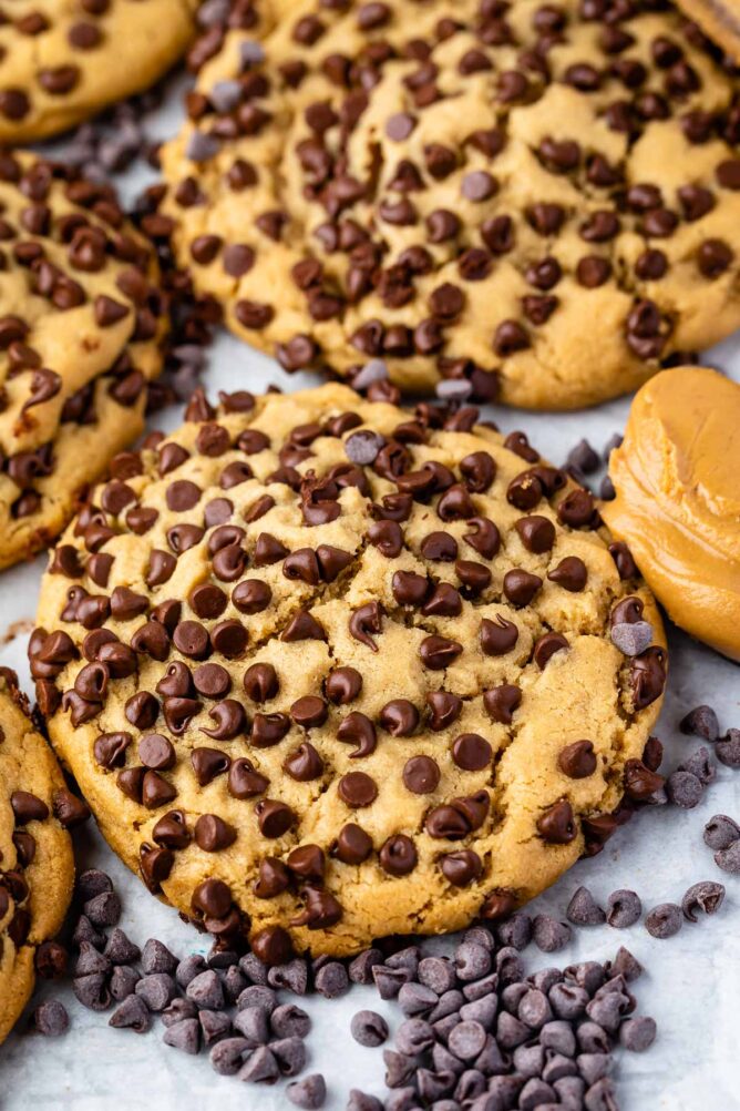 Close up overhead shot of ultimate stuffed peanut butter cookies on parchment paper surrounded by mini chocolate chips