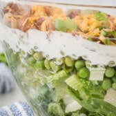 layered salad in a clear bowl showing lettuce and dressing and meat and cheese with words on the photo