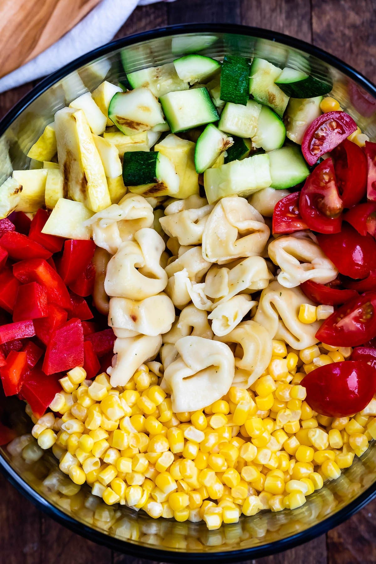 corn and zucchini and peppers and pasta and tomatoes all separated in a clear bowl