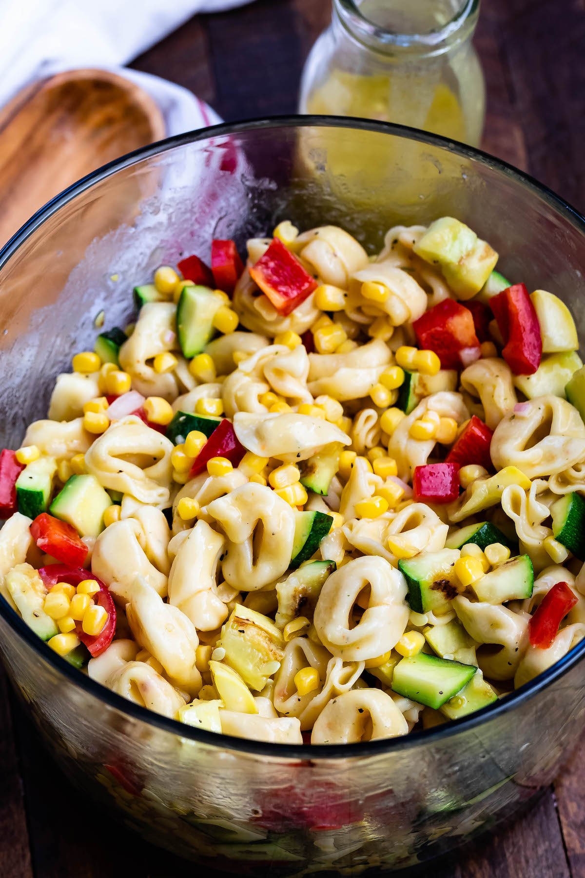 corn and zucchini and peppers and pasta and tomatoes all mixed together in a clear bowl