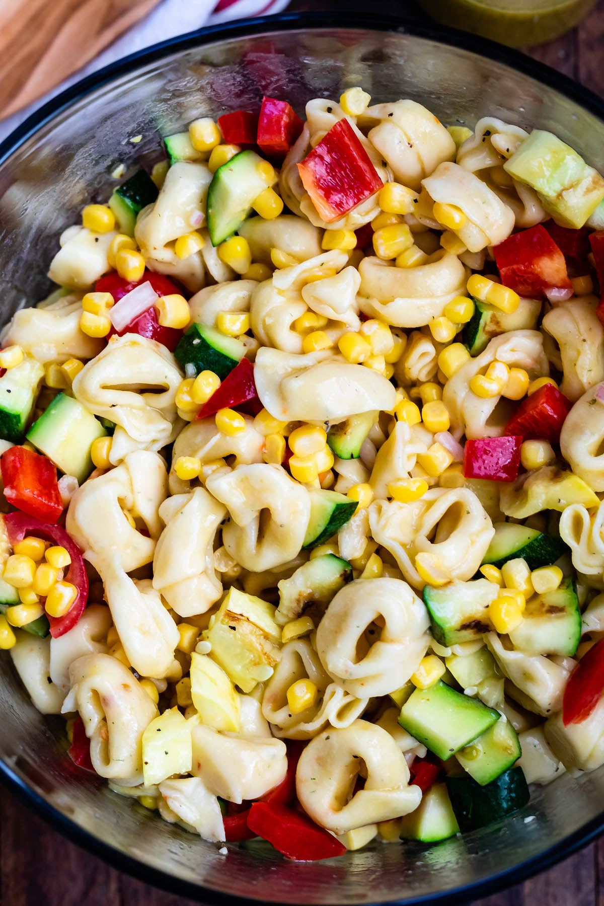 corn and zucchini and peppers and pasta and tomatoes all mixed together in a clear bowl