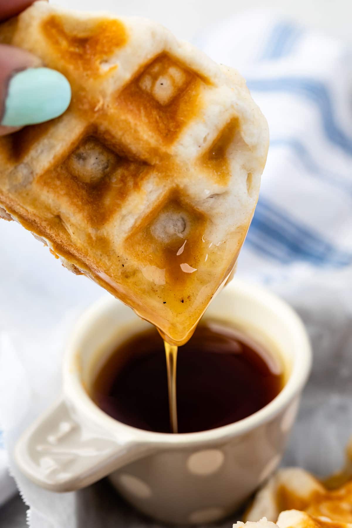 waffle being dipped into white glass filled with syrup