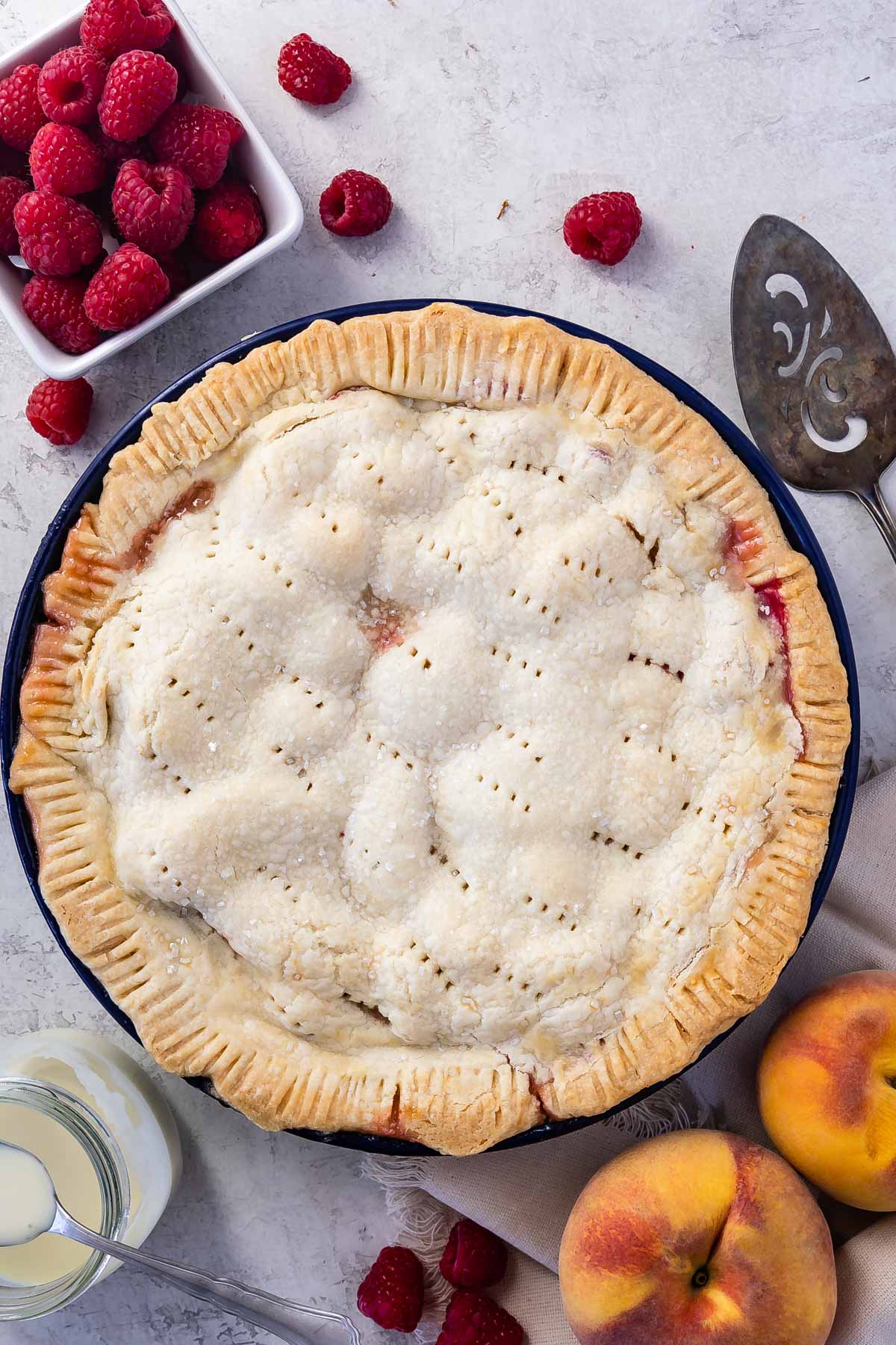 full pie with peaches and raspberries around it