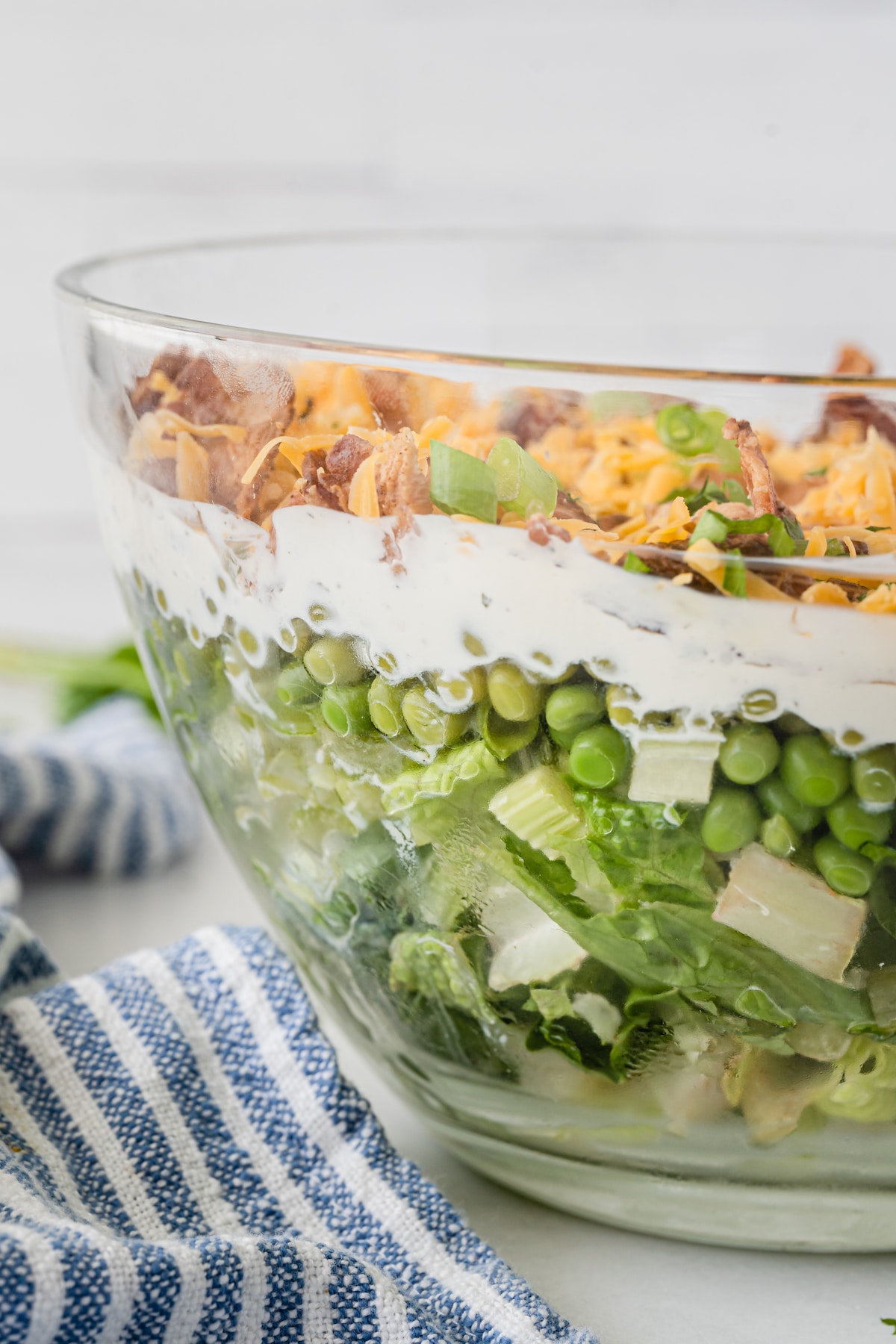 layered salad in a clear bowl showing lettuce and dressing and meat and cheese